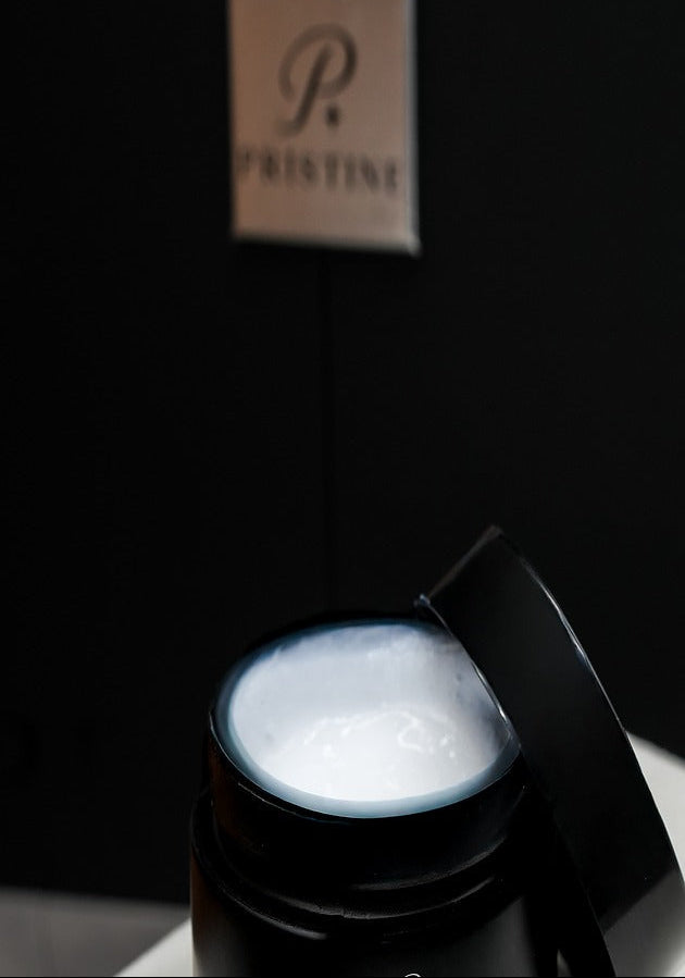 Open PRISTINE Leather Care Lotion jar showing the white lotion, with its black lid resting against the rim.