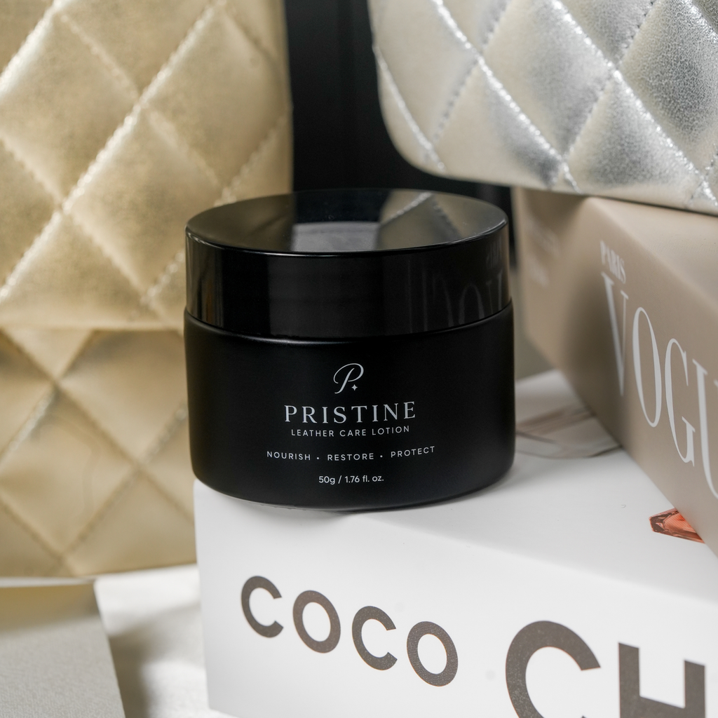 PRISTINE Leather Care Lotion on stacked fashion books with cream and silver quilted handbags.