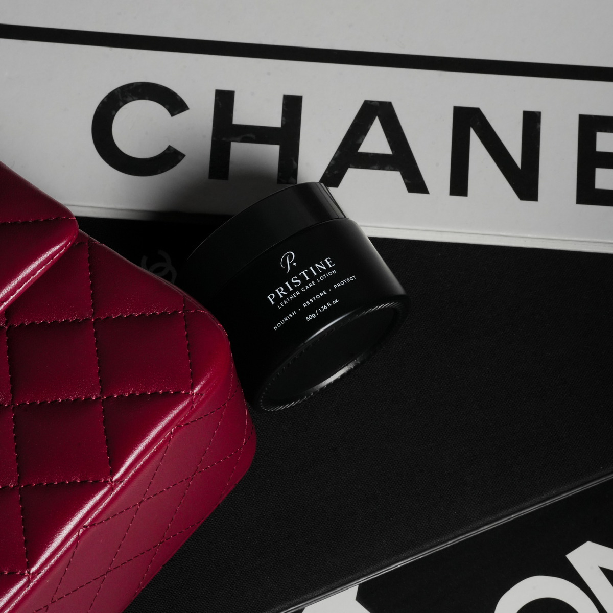 PRISTINE Leather Care Lotion jar beside a burgundy quilted handbag and fashion books.