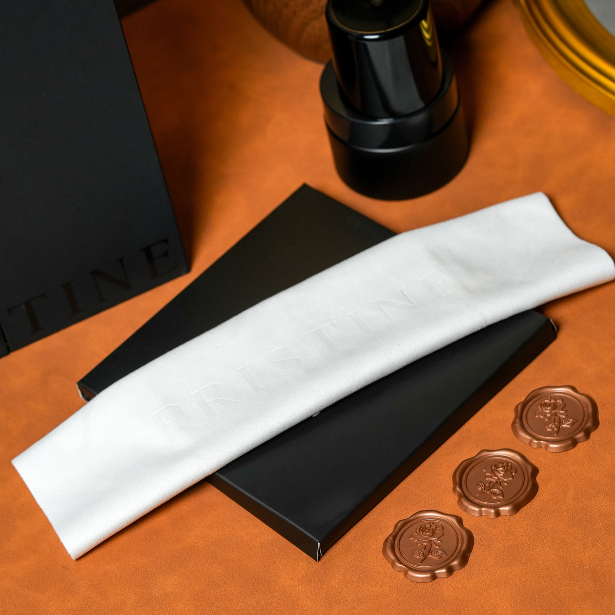 White PRISTINE care cloth laid over black packaging beside a cleaner bottle on an orange tabletop.