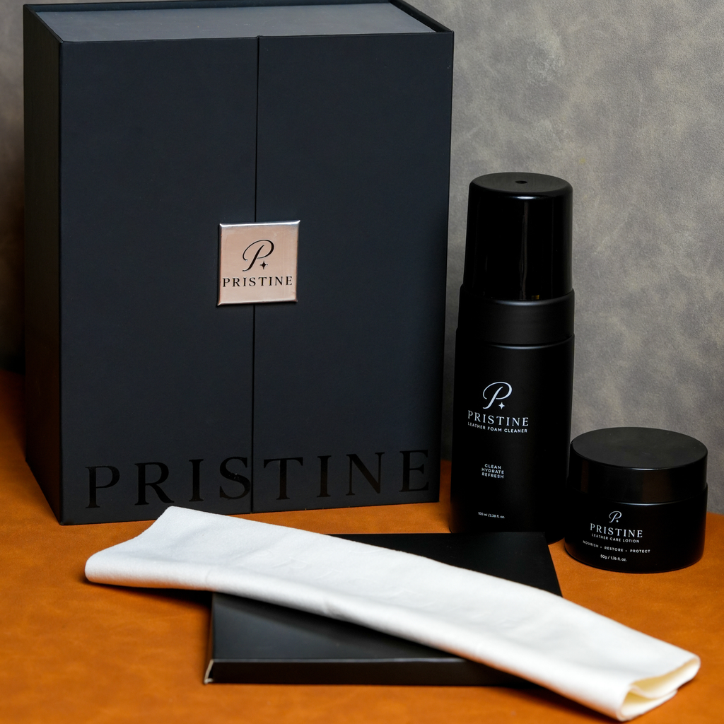 The Pristine System with cleaner, lotion, white cloth and black presentation box on an orange surface.