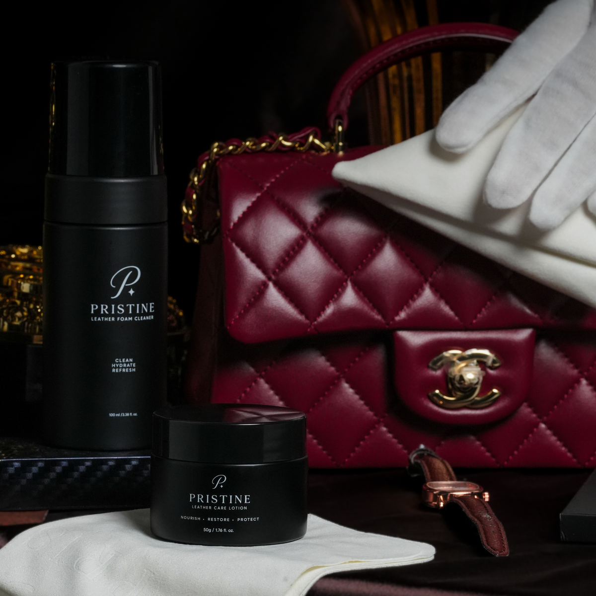 PRISTINE cleaner and lotion beside a burgundy quilted handbag being wiped with a white cloth.
