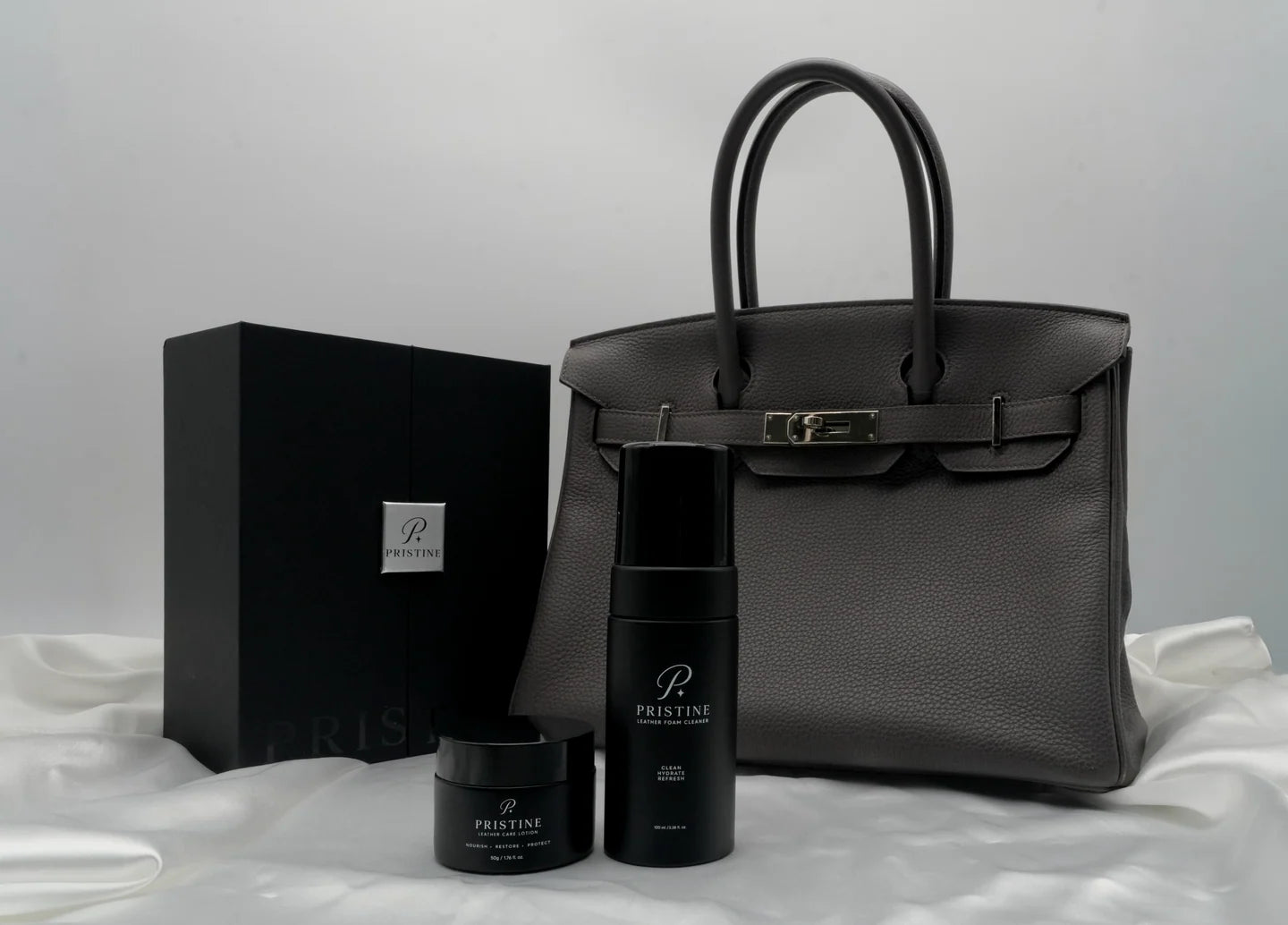 PRISTINE care products and presentation box beside a grey leather bag